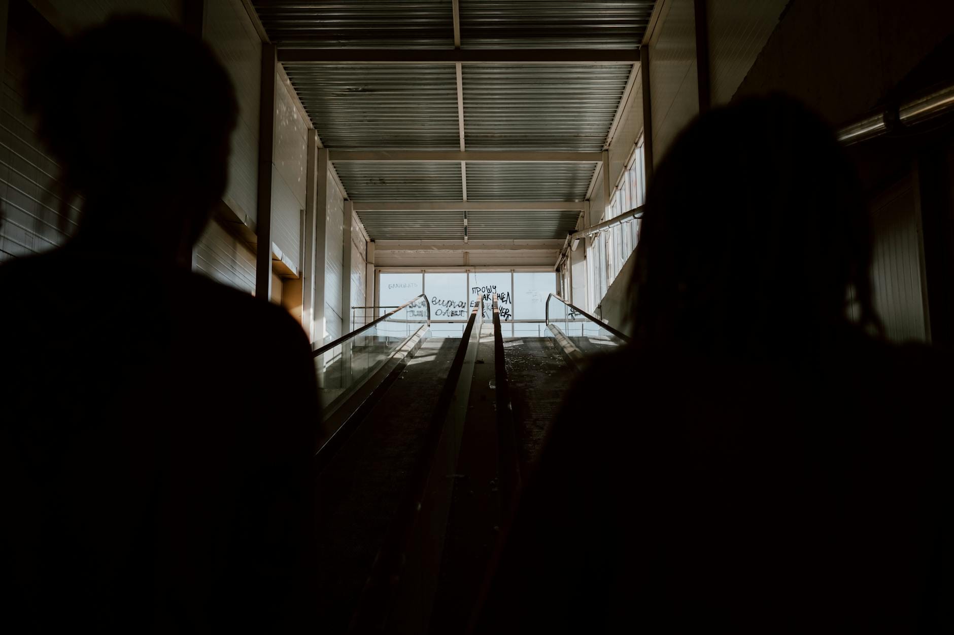 Dwie sylwetki na ruchomych schodach w ciemnym, nastrojowym wnętrzu