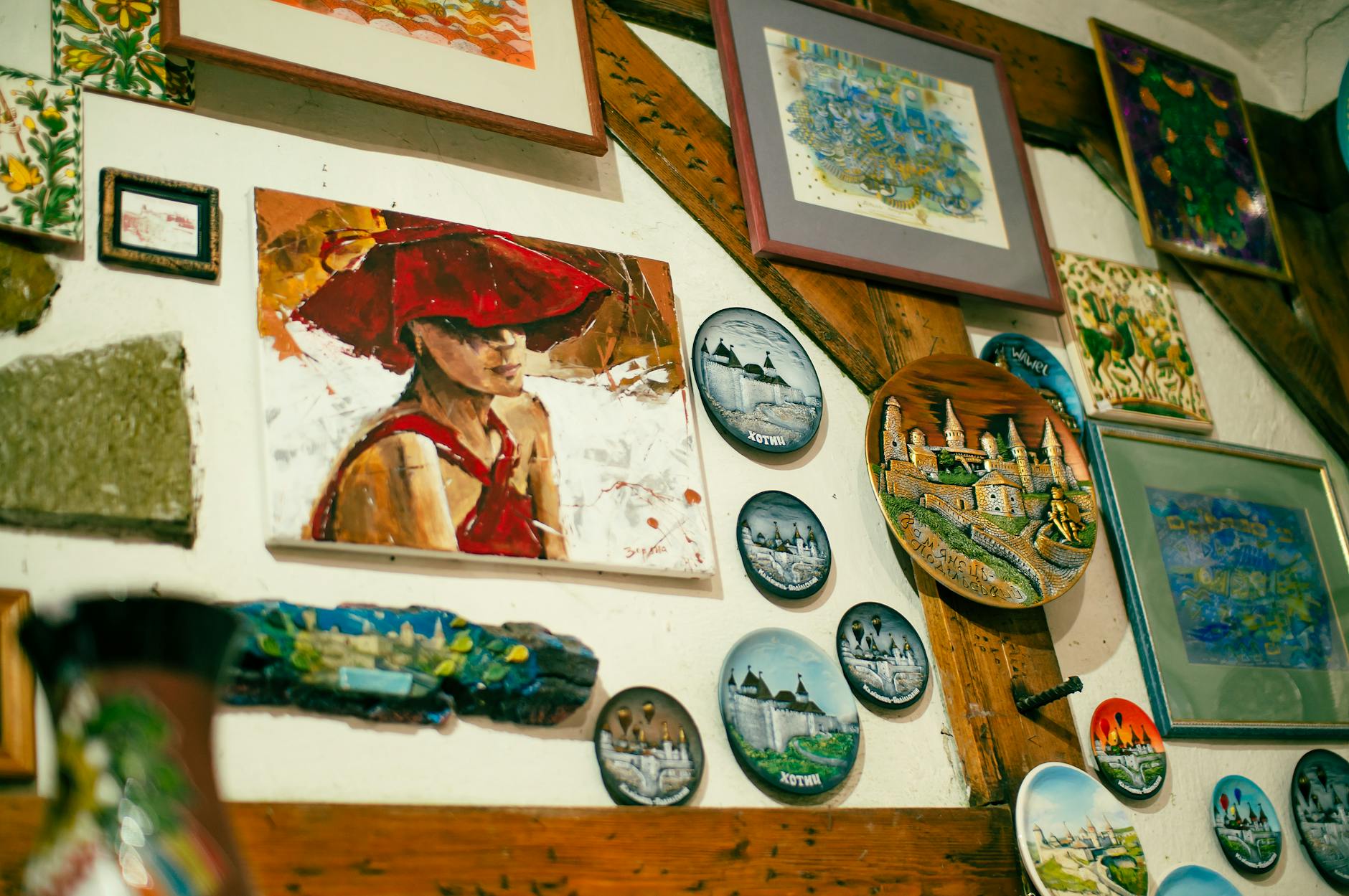 Kolorowe obrazy i ozdobne talerze tworzą galerię na drewnianej ścianie