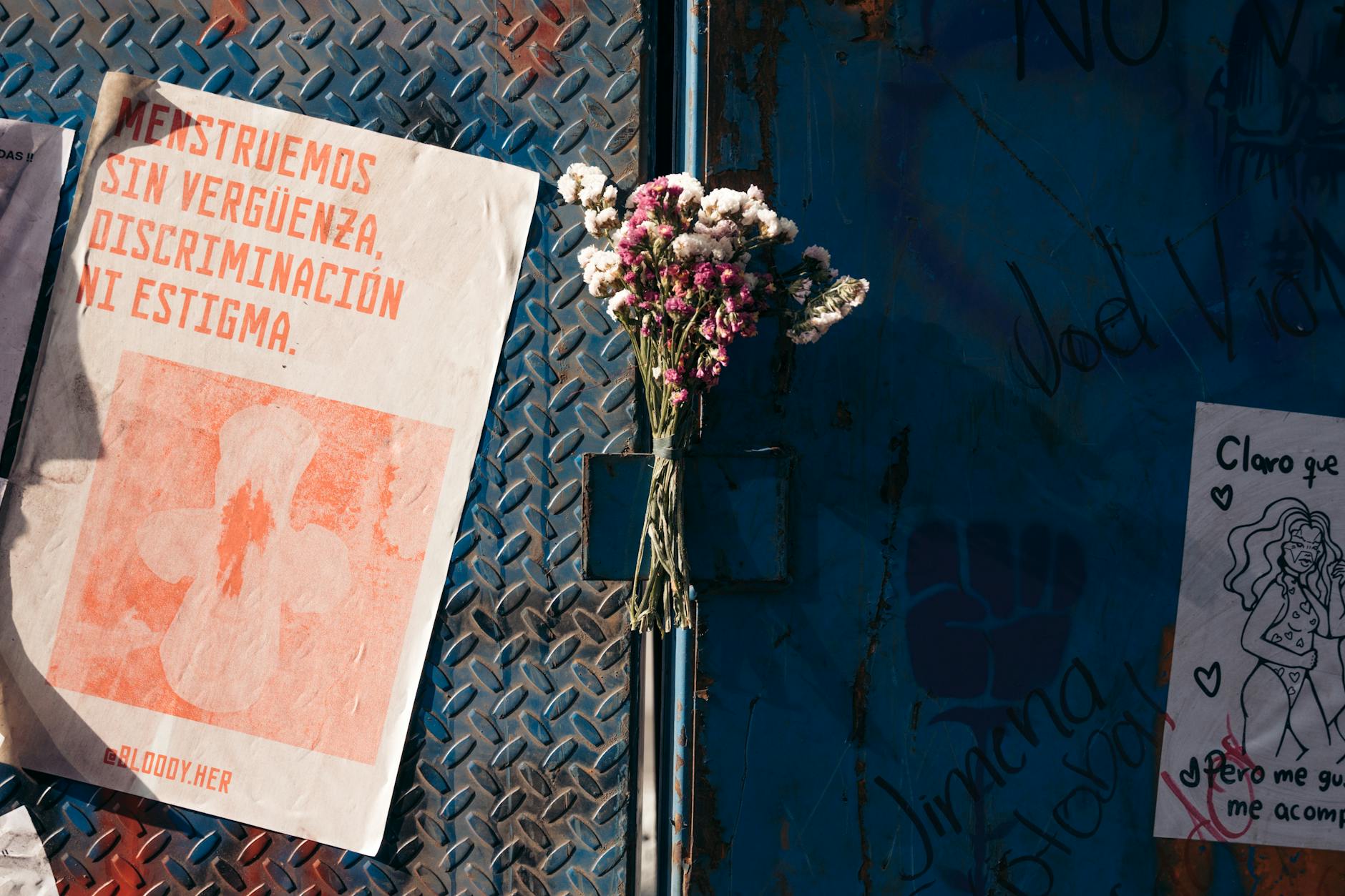 Plakaty feministyczne na miejskim murze obok bukietu kwiatów