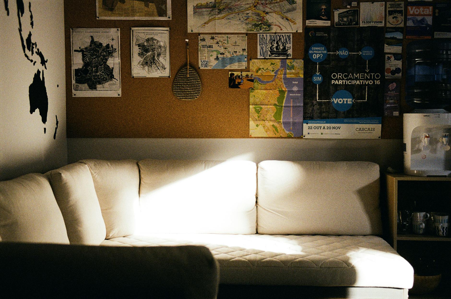 Jasny salon z kanapą i korkową ścianą ozdobioną plakatami i mapami