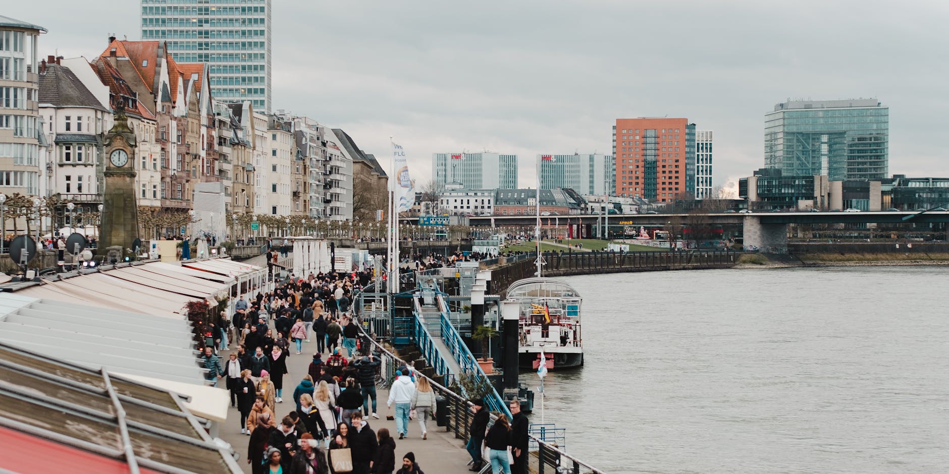 Tłumny deptak nad rzeką w mieście z zabytkową i nowoczesną zabudową