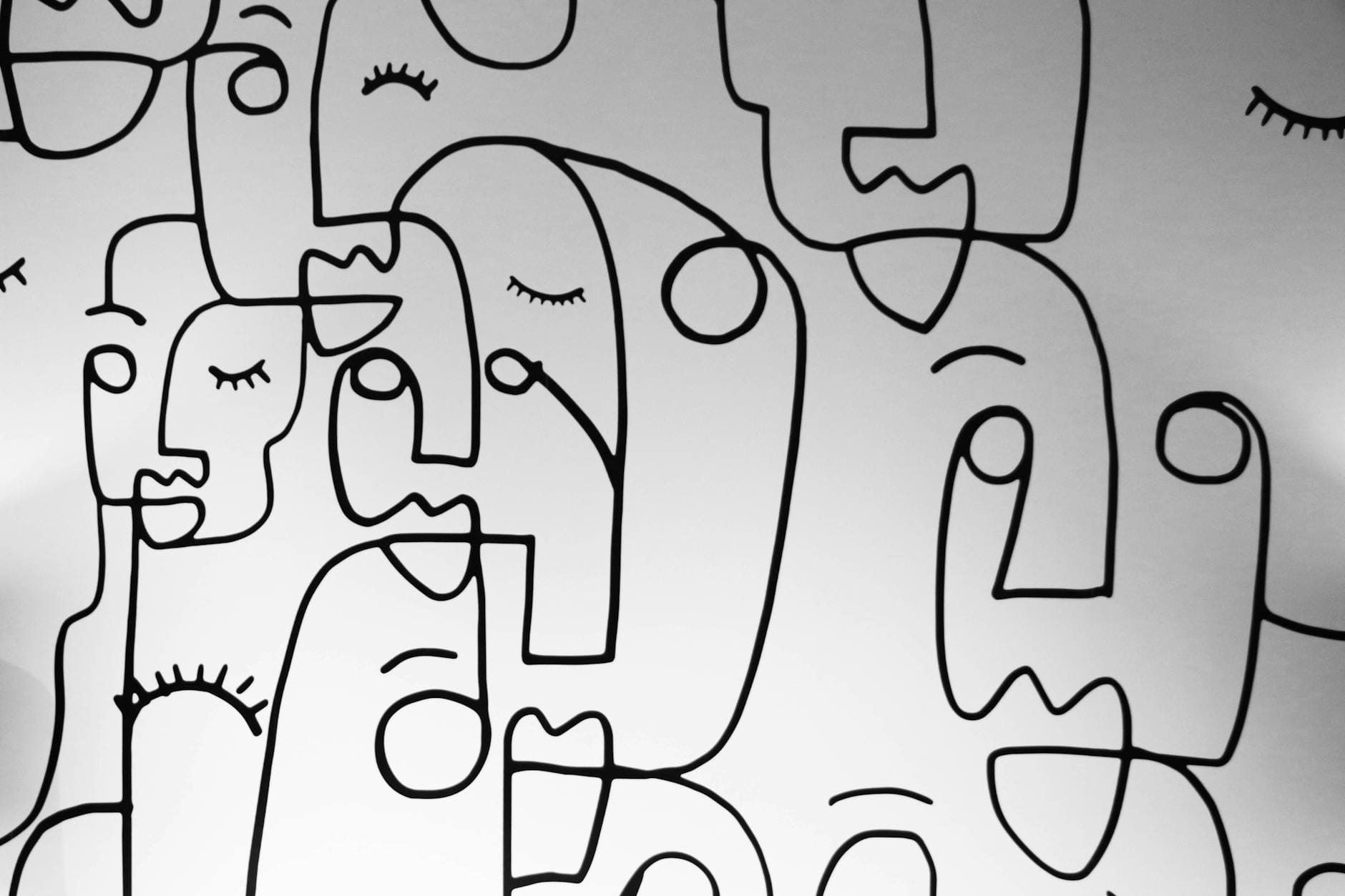 Abstrakcyjny line art z twarzami namalowanymi czarną linią na białej ścianie